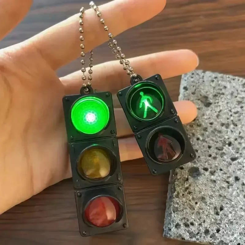 Two miniature traffic light keychains with green and pedestrian signal lights held by a hand.