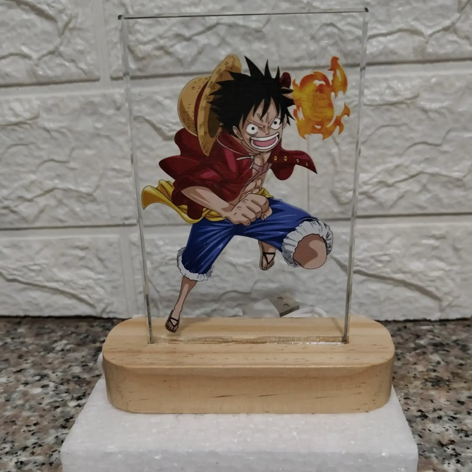 Anime character figurine on a stand with a glass cover against a textured wall background