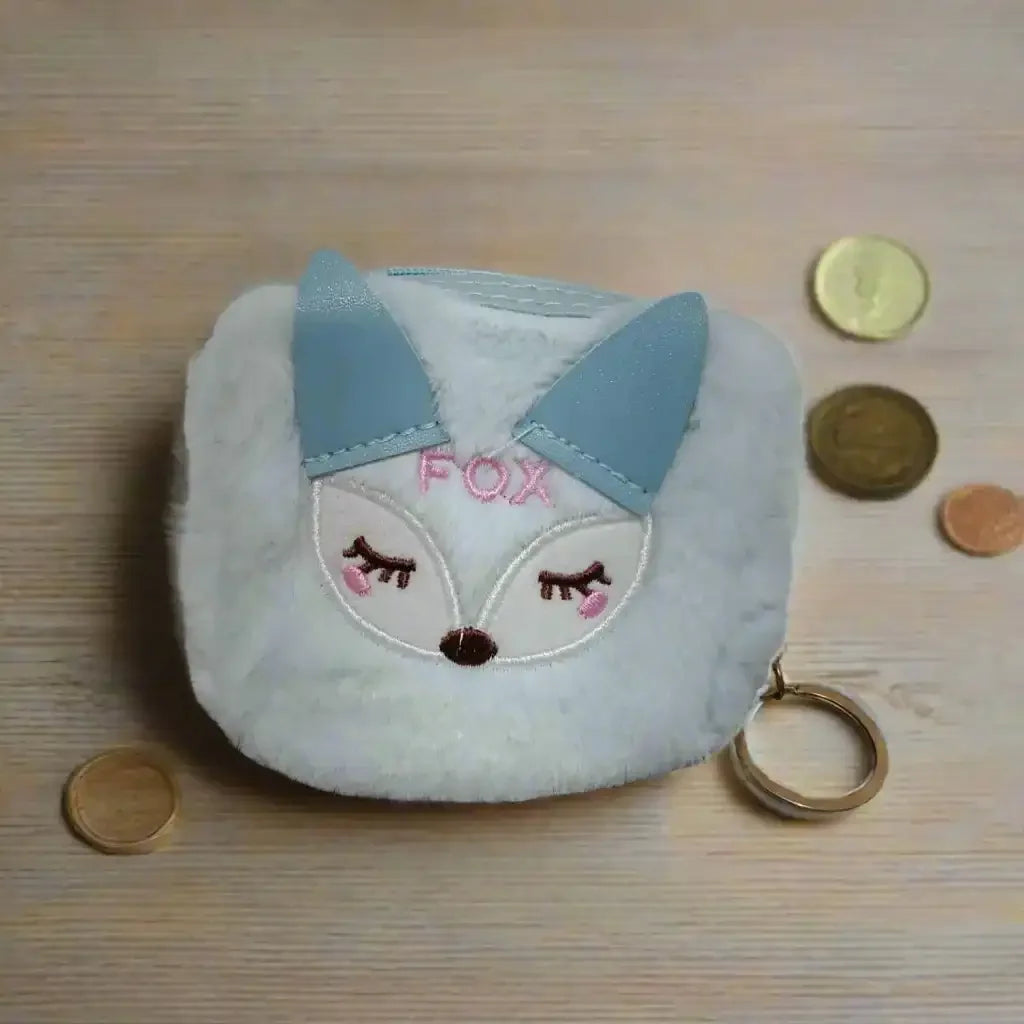 Fox-shaped coin purse with blue ears and 'FOX' embroidery on a wooden surface with coins.
