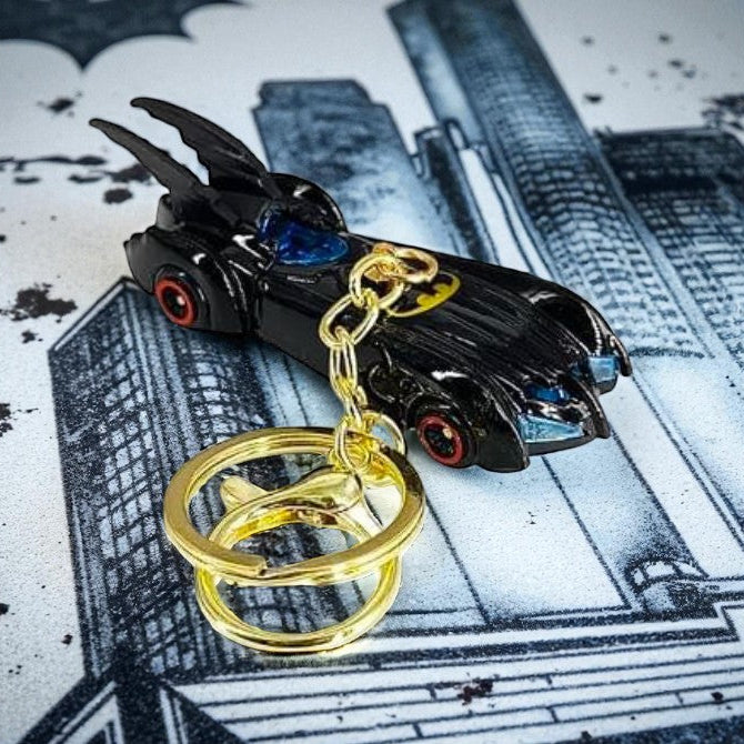 Black Batmobile keychain with gold rings on a cityscape background