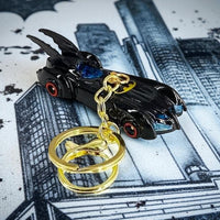 Black Batmobile keychain with gold rings on a cityscape background