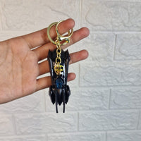 Hand holding a keychain with a gold ring against a white textured wall.