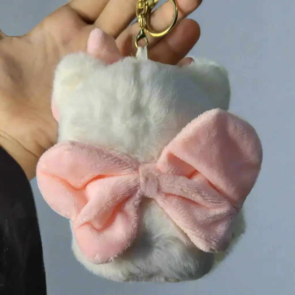 White fluffy pouch with a pink bow and gold keychain held by a hand against a light background