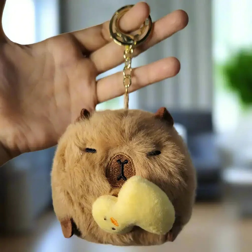 Fuzzy keychain shaped like a bear with a small yellow duck attached, held by a hand against a textured white background.