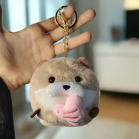 Plush keychain shaped like a bear held by a hand against a textured white wall.