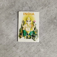 Small rectangular stamp with 'INDIA' printed on it, featuring an illustration of a deity, on a concrete surface.