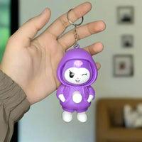 Hand holding a purple character keychain against a gray background