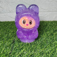 Labubu slime toy figure with purple face on grass