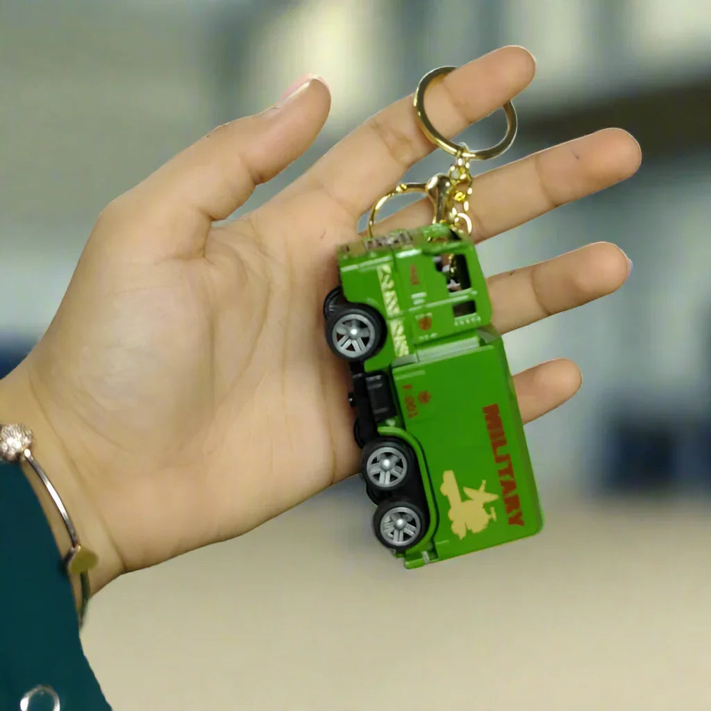 Hand holding a green toy car keychain on a grassy surface