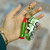 Hand holding a green toy truck keychain with red accents on a grassy surface.