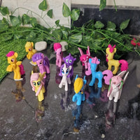 Colorful toy ponies on a reflective surface with greenery in the background