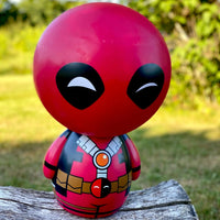 Red and black superhero figurine on a wooden log with a blurred natural background