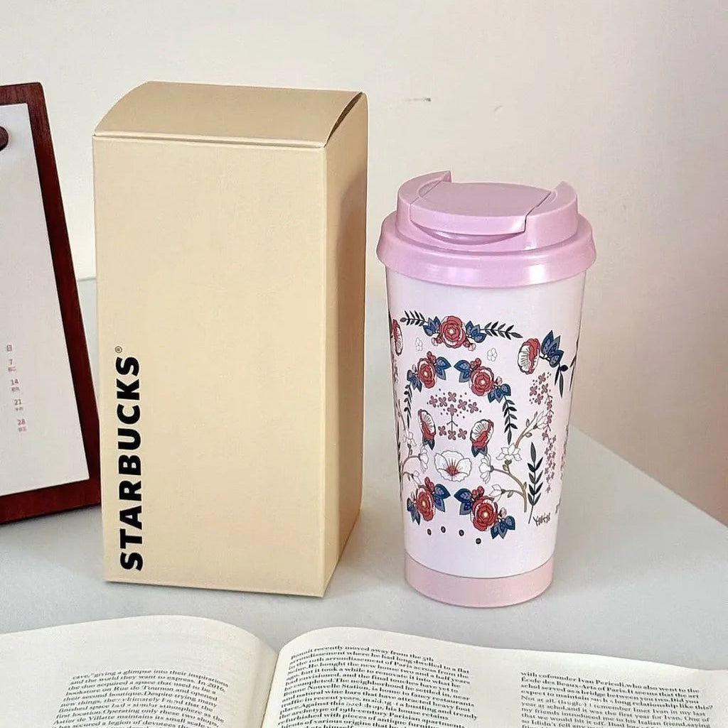 Starbucks mug with floral design and pink lid next to a beige box on a table.