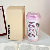 Starbucks mug with floral design and pink lid next to a beige box on a table.