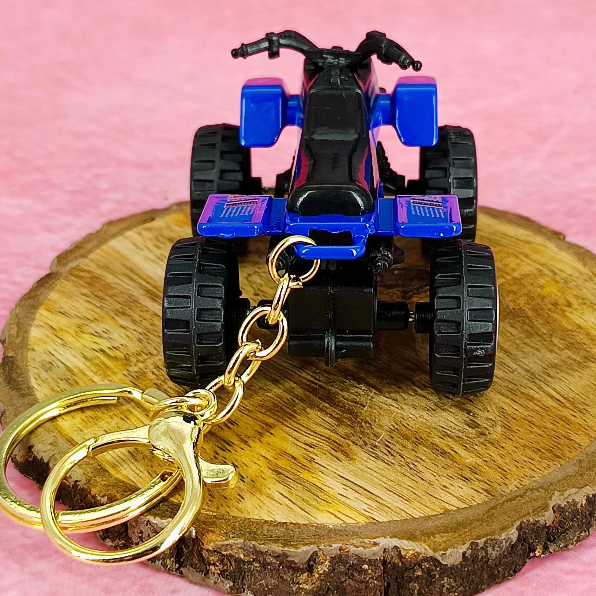 Toy ATV keychain on a wooden stand with a pink background