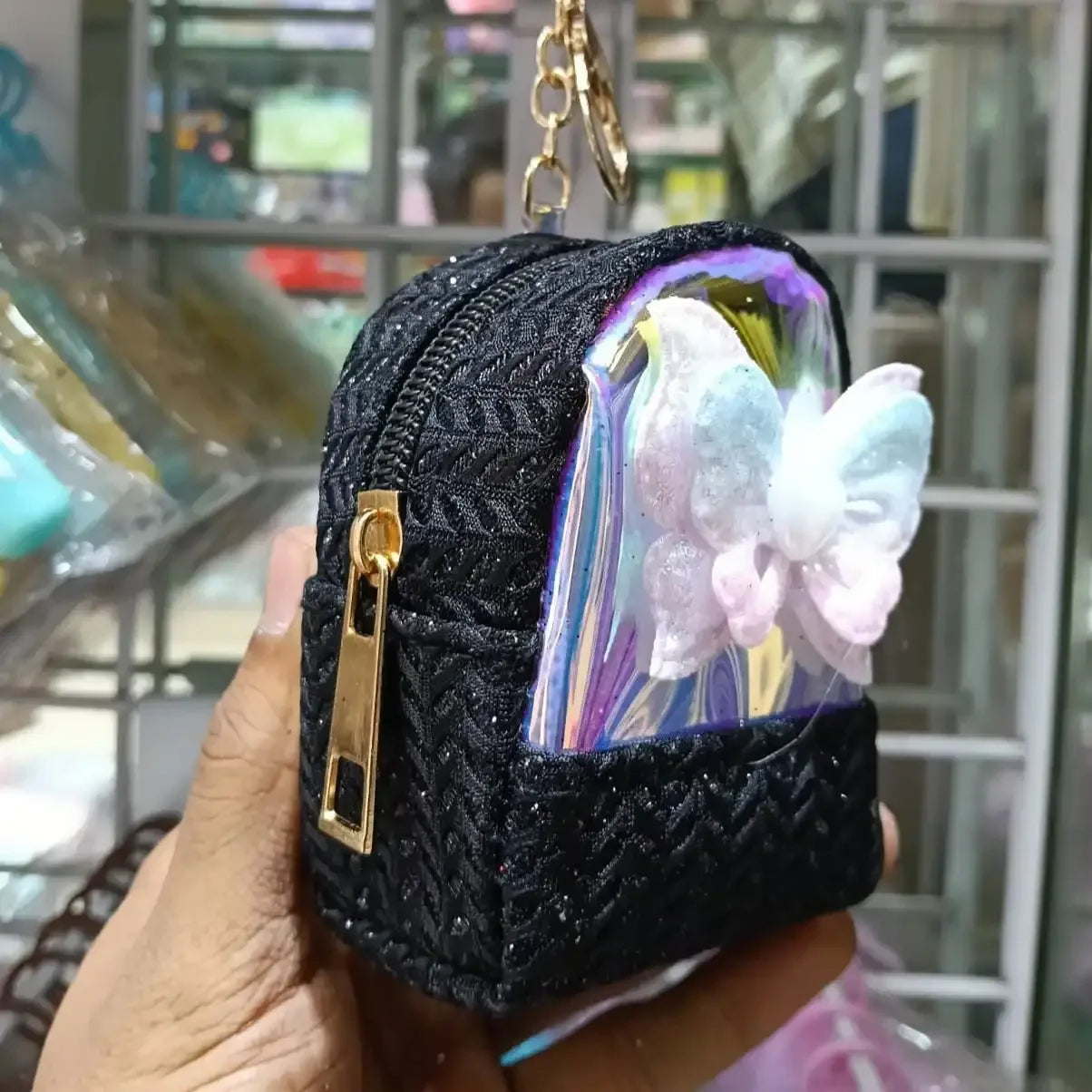 Black textured keychain pouch with a butterfly design held in front of a store interior.