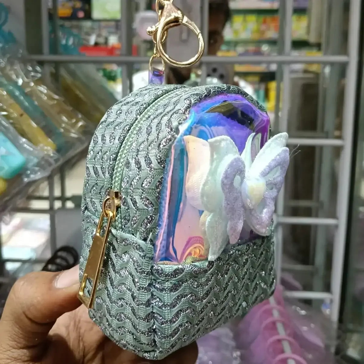 Decorative keychain with butterfly design held by a hand in a store setting