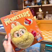 Toy figure in packaging with 'The Monsters' branding held by a person.