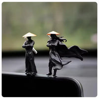 Two figurines of people wearing hats on a car's sunroof with a blurred background.