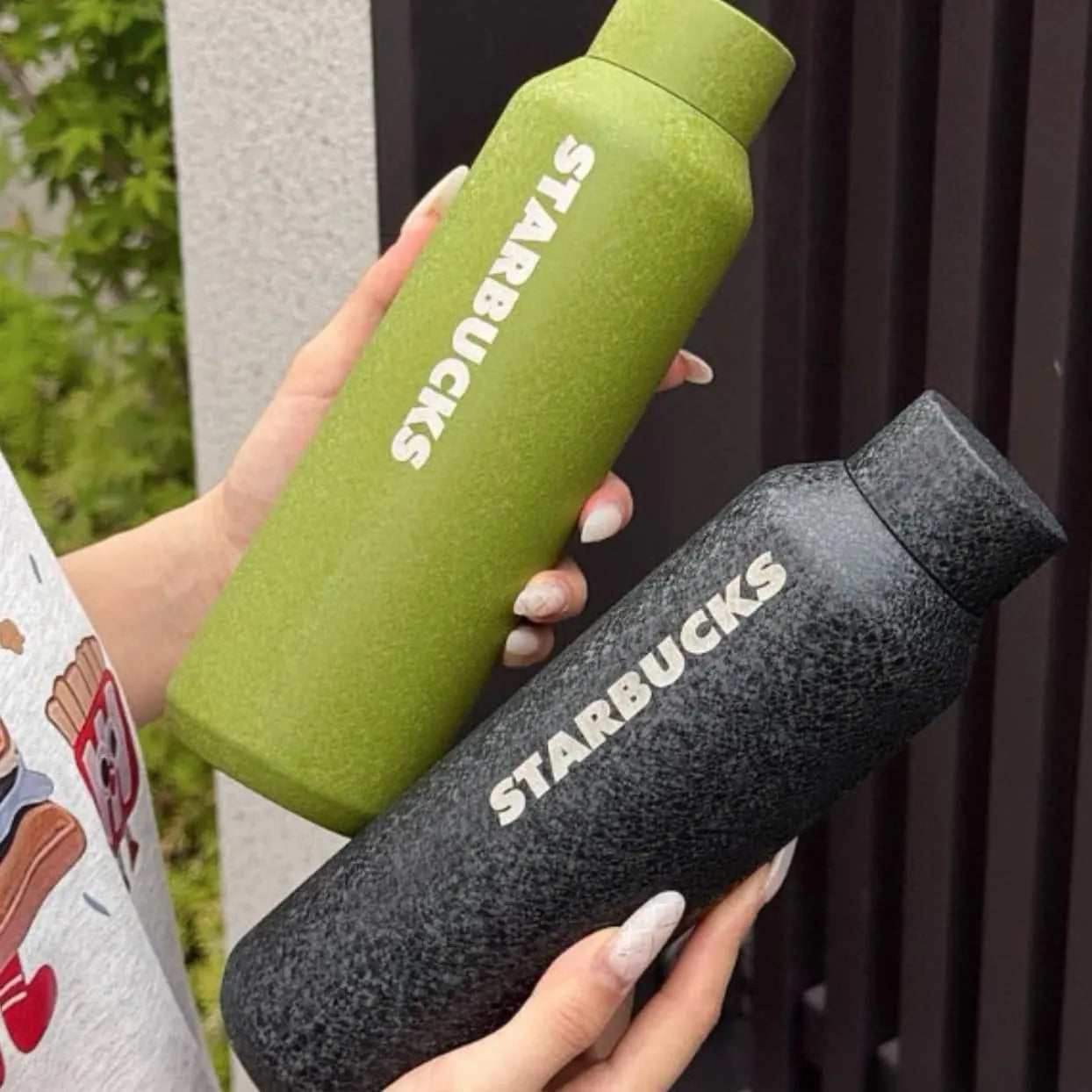 Two Starbucks water bottles, one green and one black, held by a person.