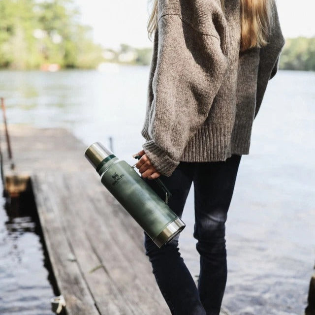 Person holding a green water bottle on a wooden dock by a lake