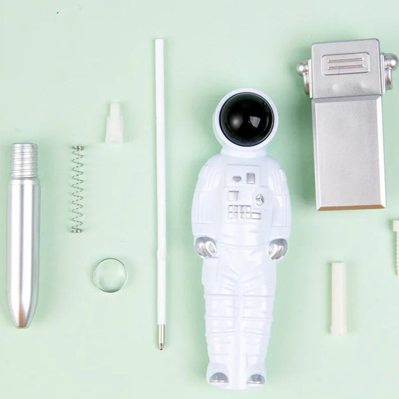 A ballpoint pen disassembled into its parts, including a white astronaut-shaped body, a silver metallic barrel, a spring, and small white plastic pieces, arranged on a pale mint green background with Chinese text and the words 'Ballpoint Pen' at the top.