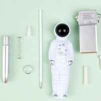A ballpoint pen disassembled into its parts, including a white astronaut-shaped body, a silver metallic barrel, a spring, and small white plastic pieces, arranged on a pale mint green background with Chinese text and the words 'Ballpoint Pen' at the top.