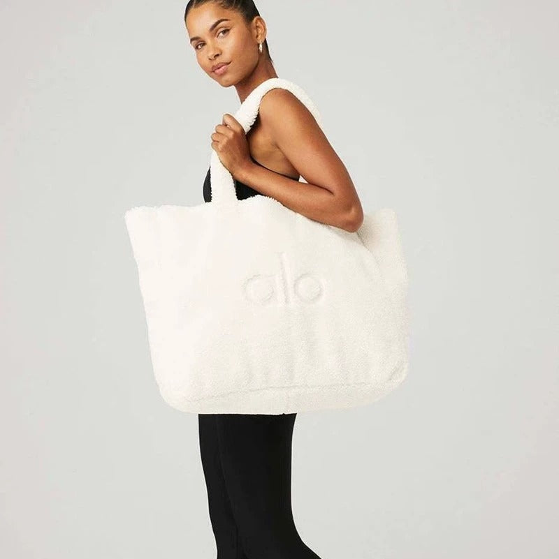 Person holding a white tote bag with a logo on a plain background
