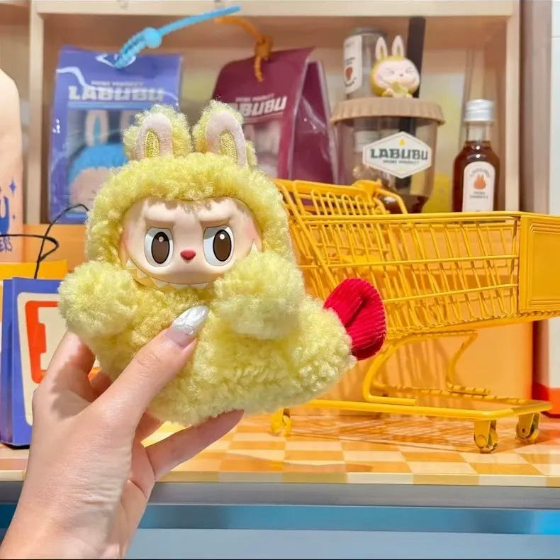Yellow plush toy with bunny ears held by a hand, with a toy shopping cart and various items in the background.