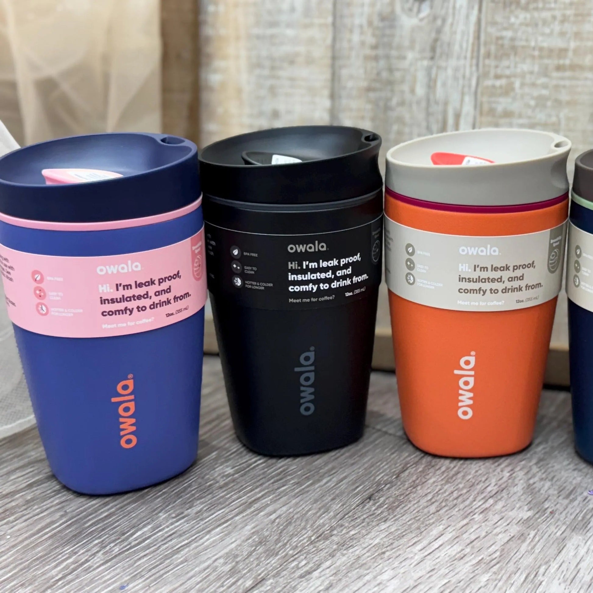 Four Owala insulated travel mugs in different colors on a wooden surface.