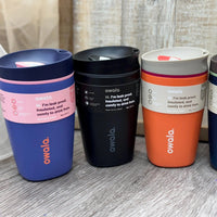 Four Owala insulated travel mugs in different colors on a wooden surface.