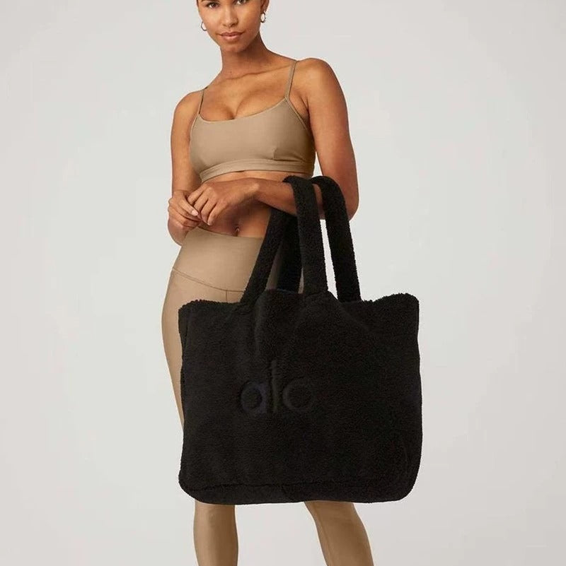 Woman holding a black tote bag with a logo on a white background