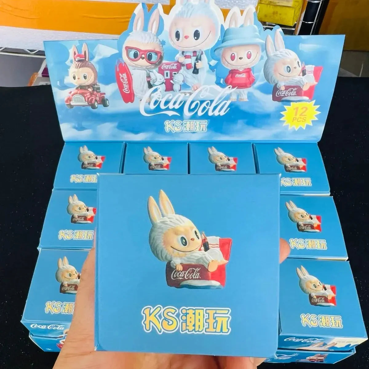 Display of Coca-Cola themed KS cartoon character boxes held by a hand.