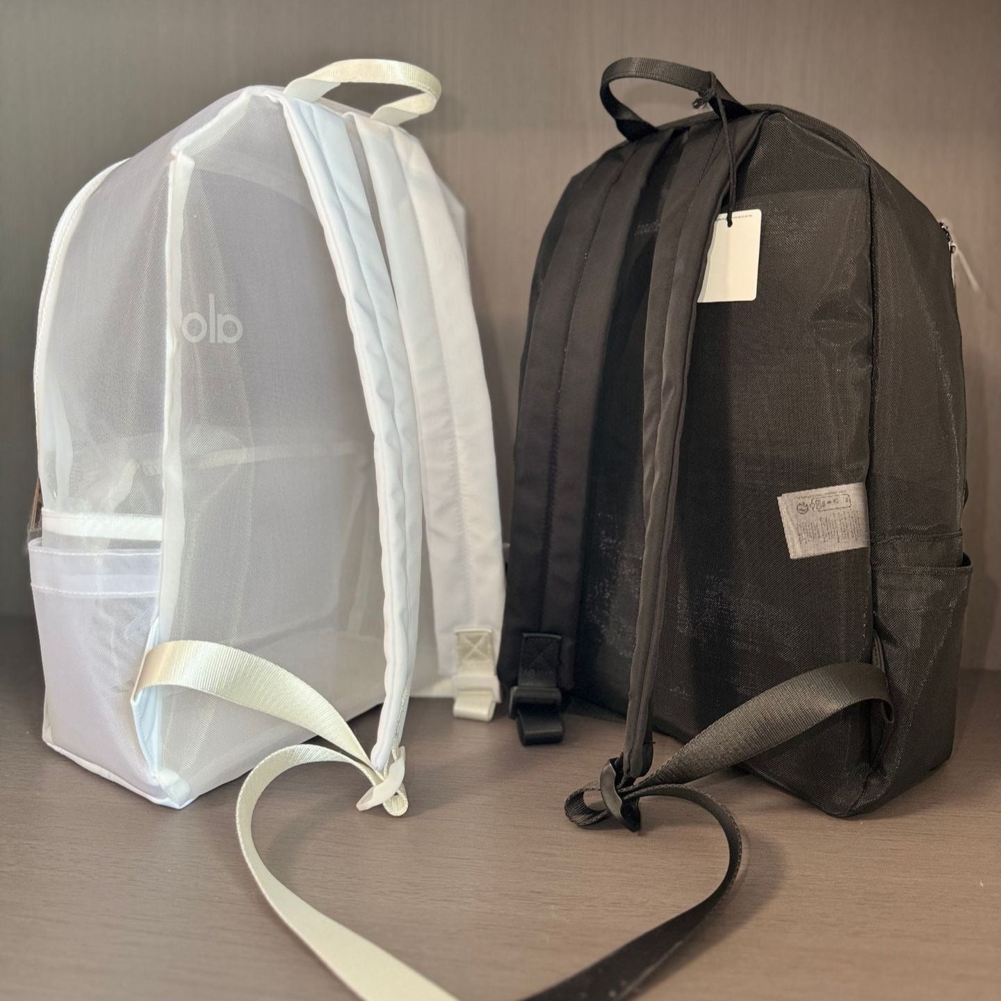 Two backpacks, one transparent and one black, on a wooden surface with a neutral background.
