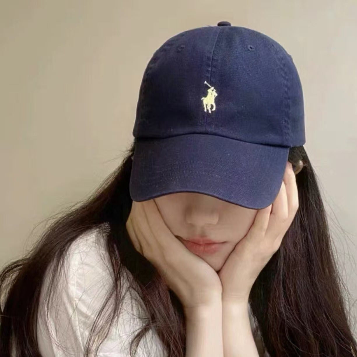 Person wearing a navy blue cap with a logo, sitting indoors.