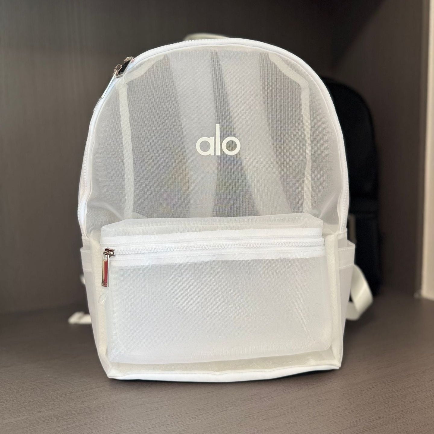 Clear backpack with 'alo' branding on a gray surface