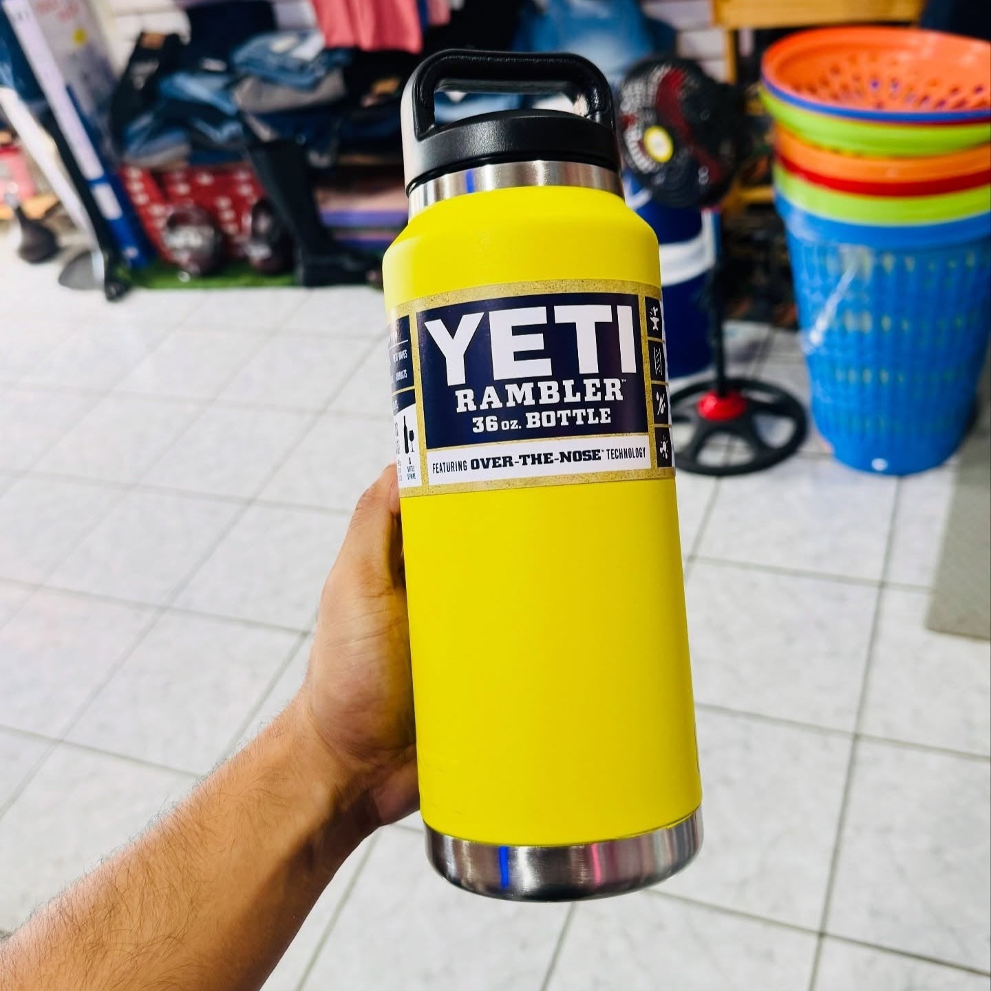 Yellow YETI Rambler bottle held by a person in an indoor setting with various items in the background.