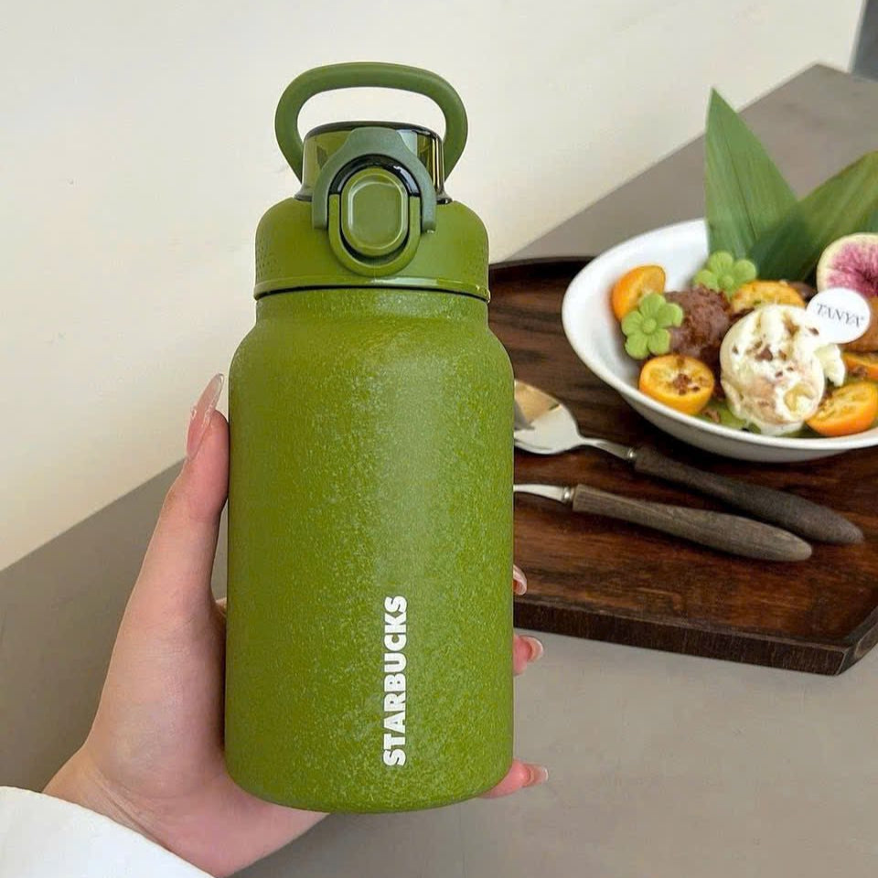Green Starbucks water bottle held by a hand with a meal in the background