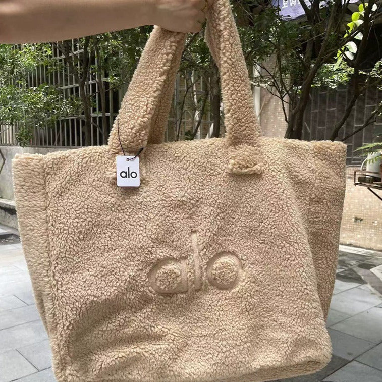 Beige fluffy tote bag with 'alo' branding held by a person outdoors.