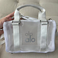 Clear handbag with 'alo' branding held by a person on a beige surface