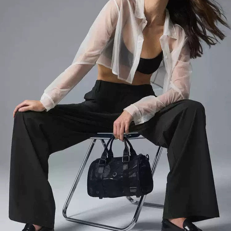 Woman sitting on a chair holding a black handbag against a gray background