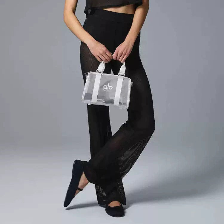 Woman holding a clear handbag with a visible brand logo against a gray background