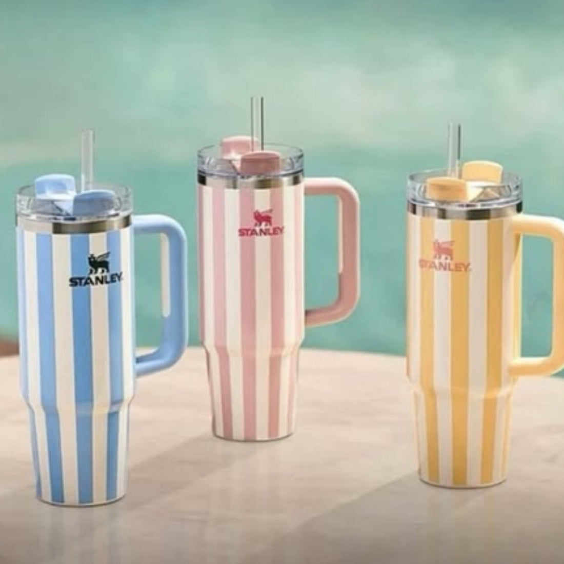 Three striped tumblers with handles on a light surface and gradient green background