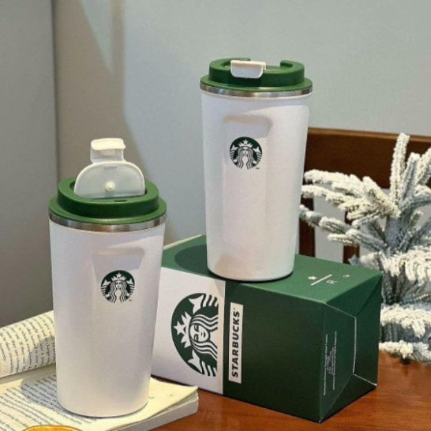 Two Starbucks tumblers with green lids on a wooden surface with a box and orange slice.