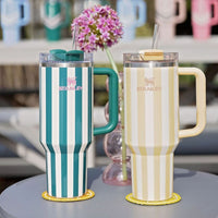 Two insulated mugs with handles on a table outdoors, surrounded by blurred outdoor furniture and decor.