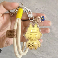 Gold labubu-shaped keychain with a clear cover held by a hand on a gray background