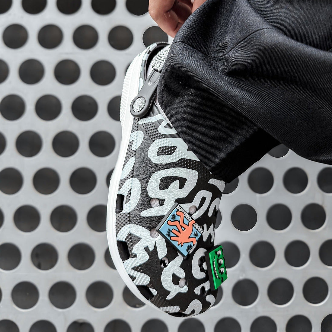 Hand zipping a black and white patterned pouch against a perforated metal background