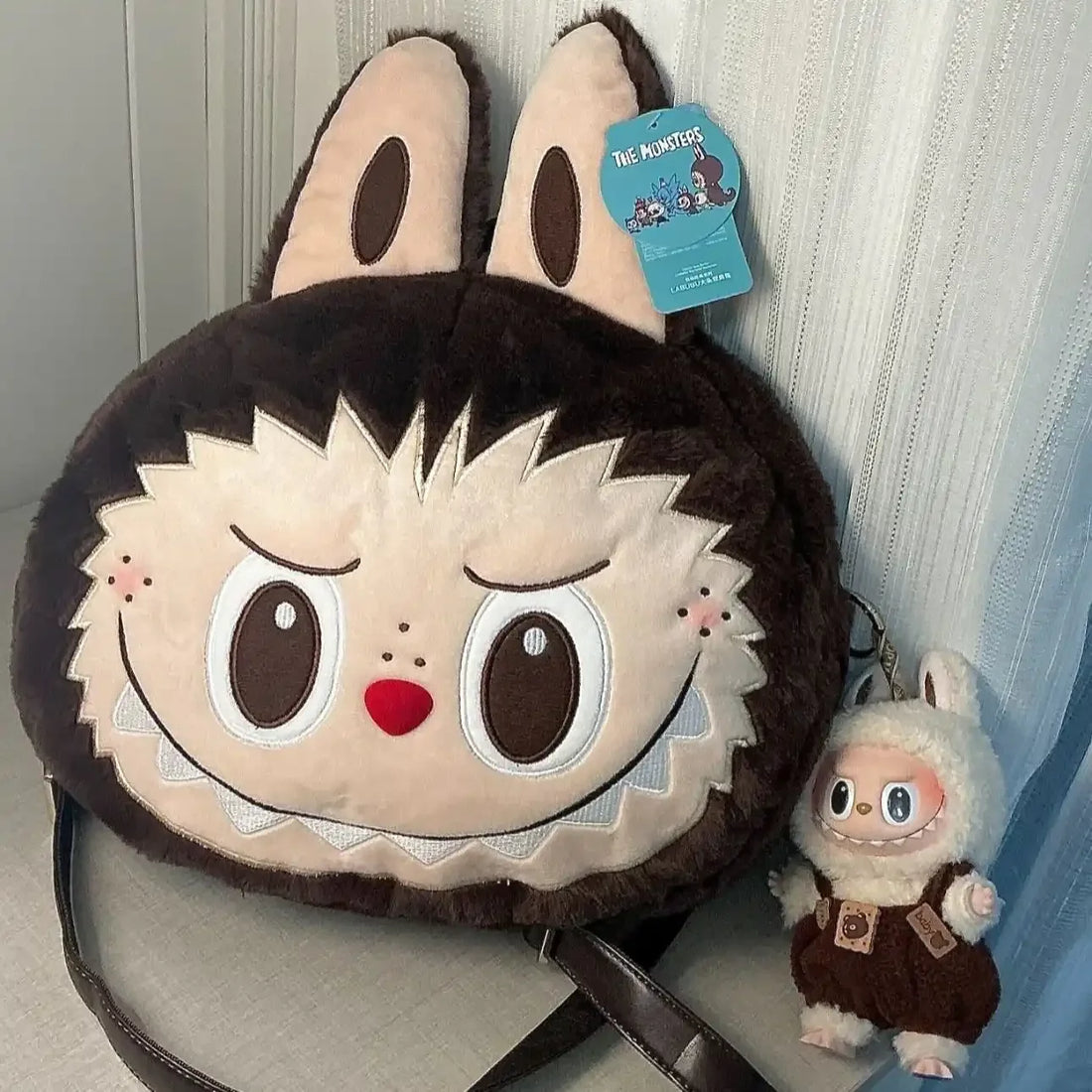 Plush bag with cartoon character face design and small plush toy attached, against a neutral background.