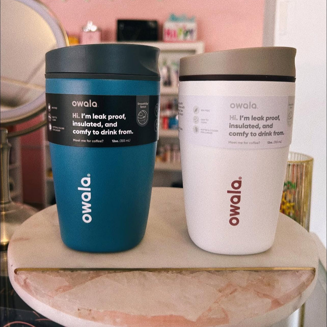 Two Owala tumblers, one blue and one white, on a marble surface with a blurred indoor background.