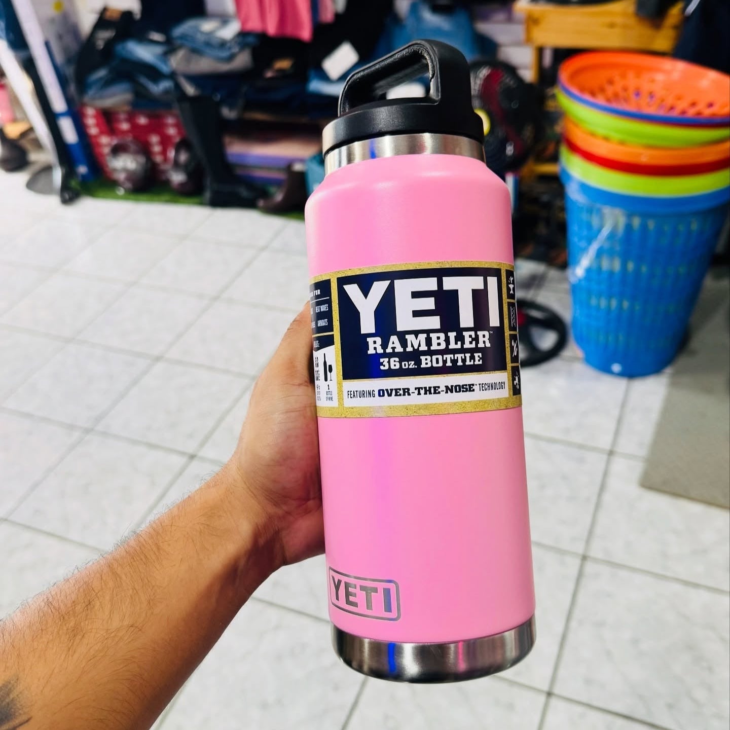 Pink YETI Rambler bottle held by a person in an indoor setting with various items in the background.